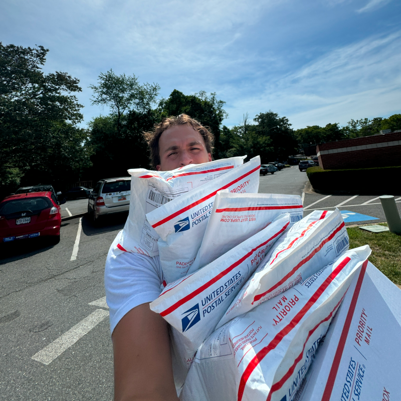 Drew carrying an armful of USPS Priority Mail packages to ship